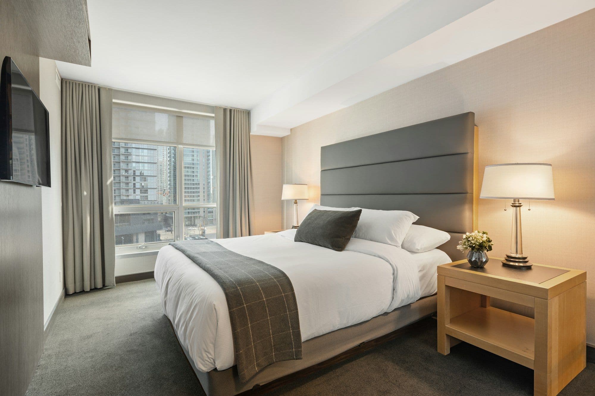 Bright hotel guest room with a made bed, curtains and carpet