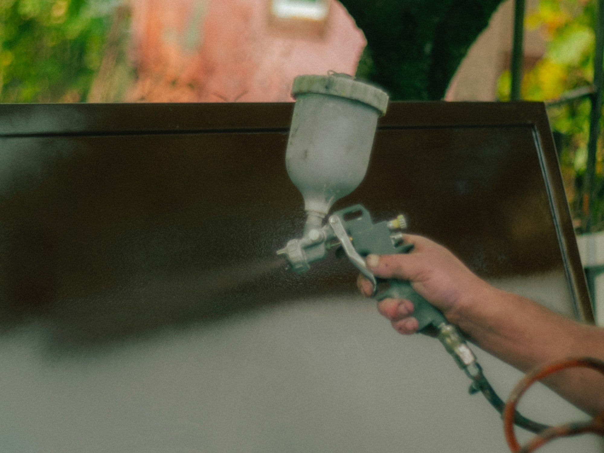 Technician calibrating a 0.5 mm HVLP spray gun to atomize 5-10 nm nano-TiO2 photocatalyst coating across a sunlit commercial wall.