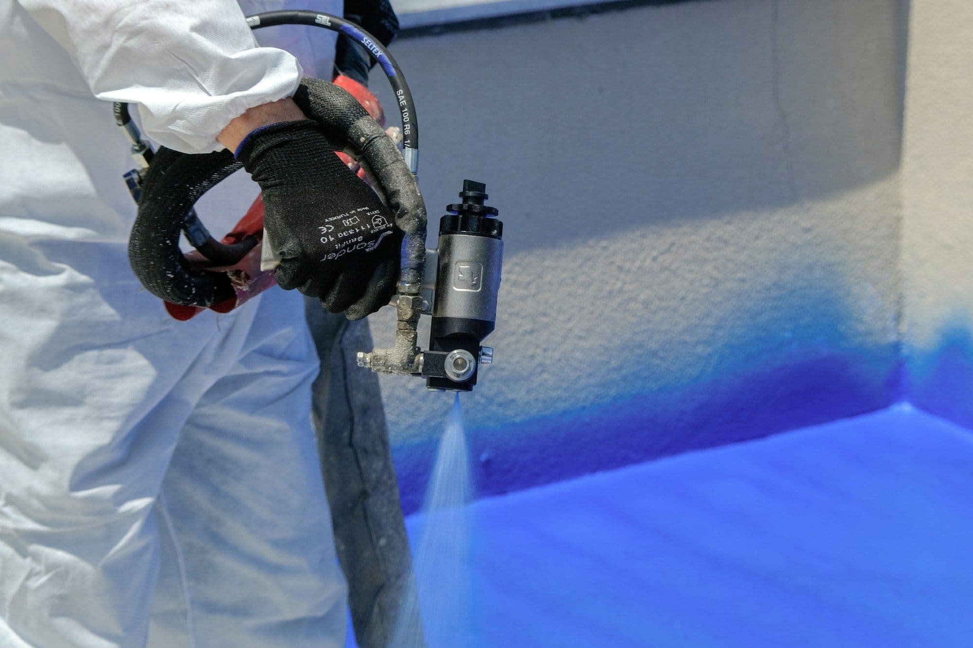 Technician in a protective suit spraying a wall with a spray gun