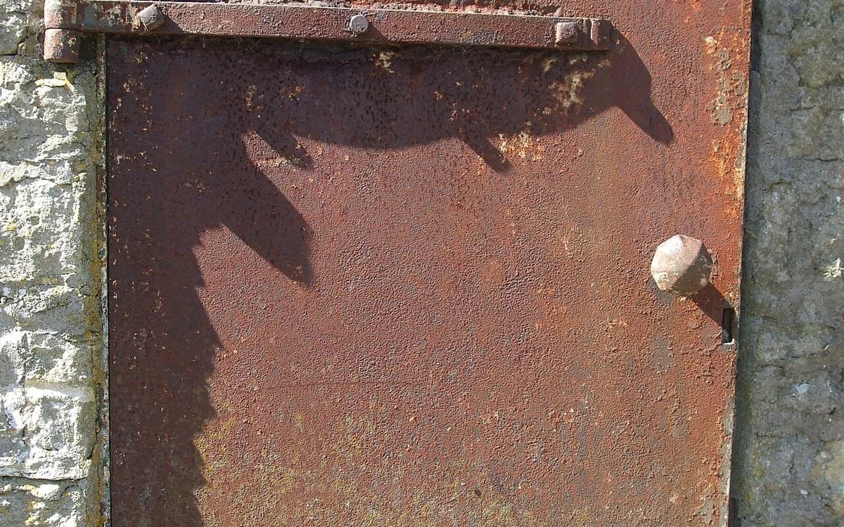 Corroded steel hinge damaged by acidic chloride exposure compared to protected hardware