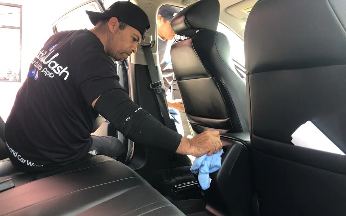 Auto detailing technician cleaning and treating a passenger vehicle cabin interior
