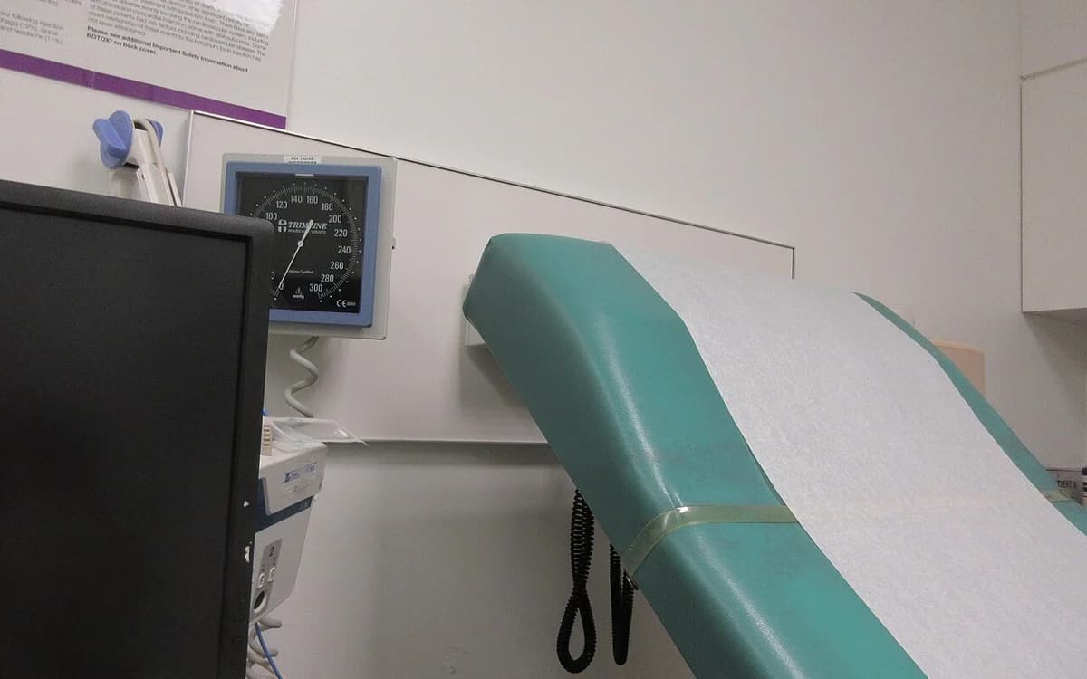 Medical clinic examination room interior with exam table, sink cabinet, and wall dispensers