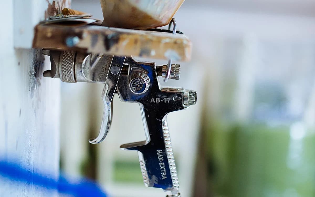 Pneumatic HVLP spray gun atomizing fine mist onto wooden cabinetry