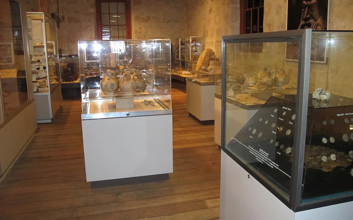 Illuminated glass museum display cases exhibiting historical ceramic and metal artifacts
