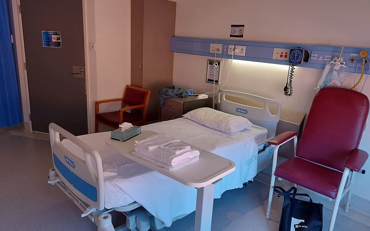 Hospital inpatient ward room with patient bed, medical wall console, and overhead LED lighting