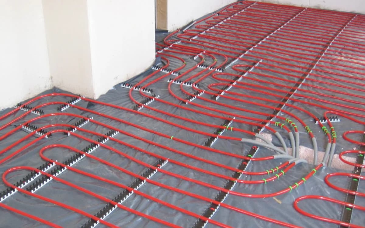 Hydronic underfloor heating pipes laid across a residential floor slab before wood flooring installation